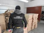 Umundurowany funkcjonariusz Służby Celno-Skarbowej stoi przed pudełkami kartonowymi wypełnionymi papierosami.