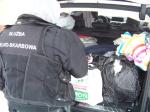 Funkcjonariusz Służby Celno-Skarbowej przed otwartym bagażnikiem auta, w bagażniku torby foliowe.