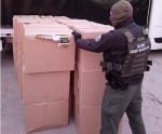 Funkcjonariusz Służby Celno-Skarbowej stoi przed kartonowymi pudłami i ogląda zawartość jednego, rozerwanego pudełka.