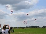 Na zdjęciu pokaz spadochronowy. Pięciu skoczków wykonuje skok spadochronowy na spadochronach w kolorze barw polskiej flagi.