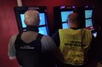 Dwaj funkcjonariusze Służby Celno-Skarbowej stoją przed automatami do gier hazardowych w pomieszczeniu.  