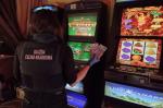 Funkcjonariuszka stoi przed automatami do gier hazardowych i trzyma w ręku banknoty.