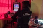 Funkcjonariuszka stoi przed automatami do gier hazardowych i trzyma w ręku torebkę foliową z brązową substancją.