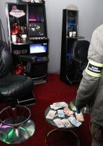 Funkcjonariusz stoi przed automatami w punkcie z nielegalnymi grami hazardowymi. Przed nim stolik z pieniędzmi.