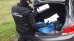 Na zdjęciu umundurowany funkcjonariusz Służby Celno-Skarbowej ogląda papierosy w bagażniku auta.  