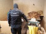 Umundurowany funkcjonariusz Służby Celno-Skarbowej stoi obok maszyny do cięcia tytoniu i nielegalnie wyprodukowanego tytoniu.