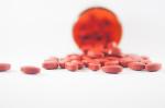 Na zdjęciu przewrócona czerwona fiolka, z której wysypują się czerwone tabletki
